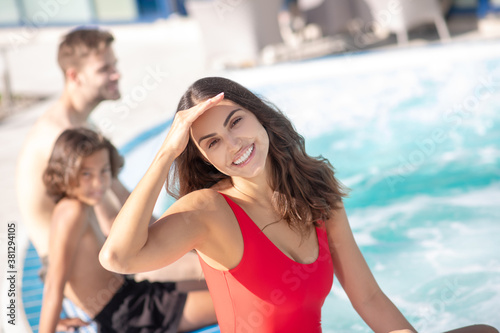 Mom in red swimming suit sitting by pool with her son and husband © zinkevych