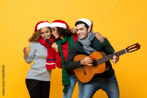 Happy three diverse friends having party singing and celebrating Christmas in yellow studio background
