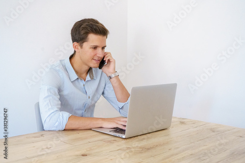 young man sitting with laptop talking on the phone