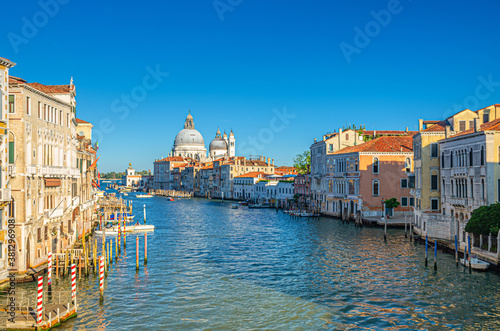 Venice cityscape with Grand Canal waterway Canal Grande in historical city centre. Santa Maria della Salute Roman Catholic church on Punta della Dogana, blue sky background. Veneto Region, Italy. © Aliaksandr