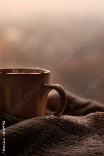 Steaming coffee cup and knitted sweater on a blurred background. Beige colors, autumn mug, autumn coffee. Banner space mock up for adding text.