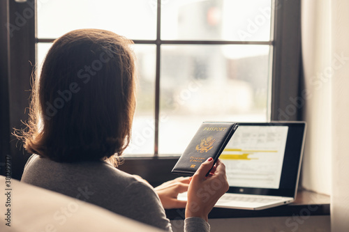 Woman holding passport filling visa application form on the laptop. Online and home work concept.