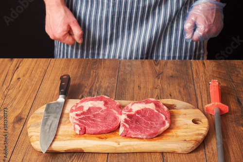 Rib eye steak on a wooden board. Professional butcher in black and white apron. Meat industry production
