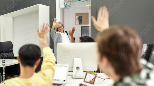 Cheerful aged woman, senior intern waving, saying goodbye to her young colleagues while leaving office after first day at work photo