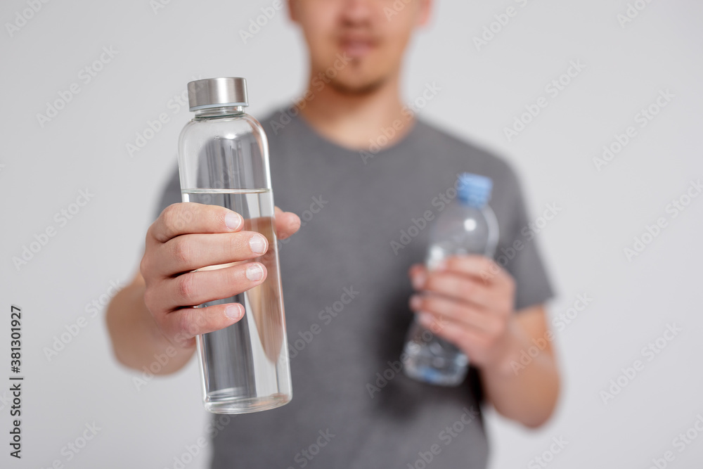 zero waste and eco friendly concept - man comparing water in reusable glass and plastic bottle over grey background zero waste and eco friendly concept - man comparing water in reusable glass and plastic bottle over grey background