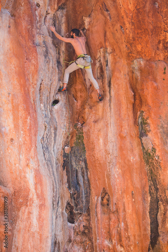 A strong man climbs a beautiful orange rock.