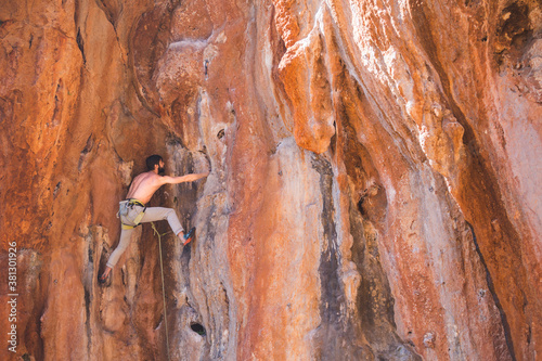 A strong man climbs a beautiful orange rock.