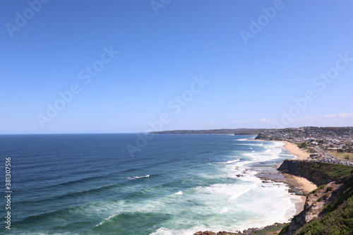Beach life. This is a landscape of Bar beach located in Newcastle NSW Australia. Blue sky, blue and white crystal surf waves, white picket fence, green hills.
