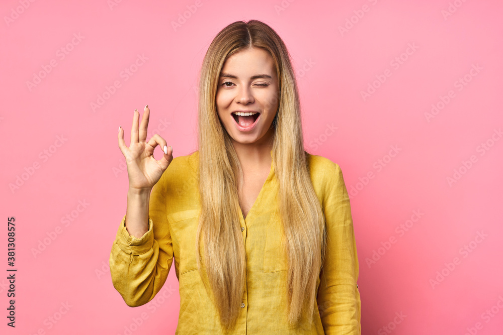 Closed eyes on portrait of sweet cute blonde girl, ok sign with fingers, isolated on pink background. Advertising concept.