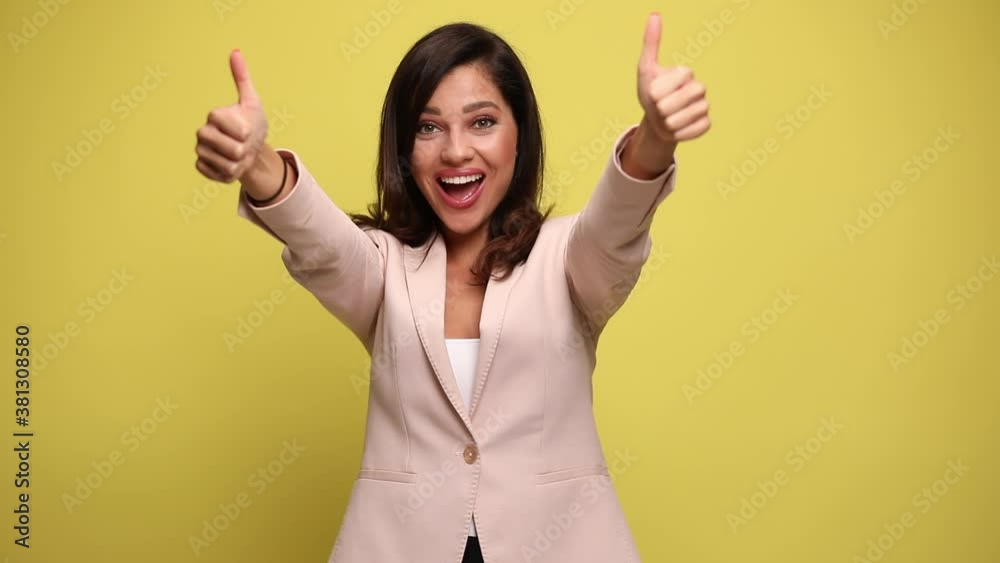 beautiful businesswoman smiling at the camera and giving a thumbs up with both her hands on yellow background beautiful businesswoman smiling at the camera and giving a thumbs up with both her hands on yellow background