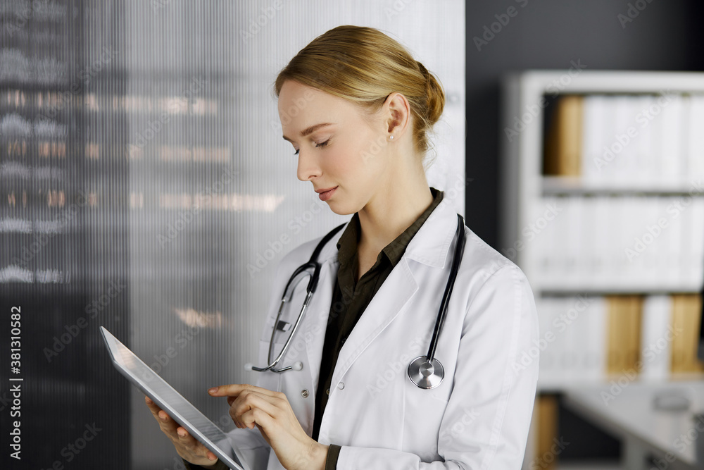 Friendly smiling female doctor using tablet computer in clinic. Perfect medical service in hospital. Medicine concept Friendly smiling female doctor using tablet computer in clinic. Perfect medical service in hospital. Medicine concept