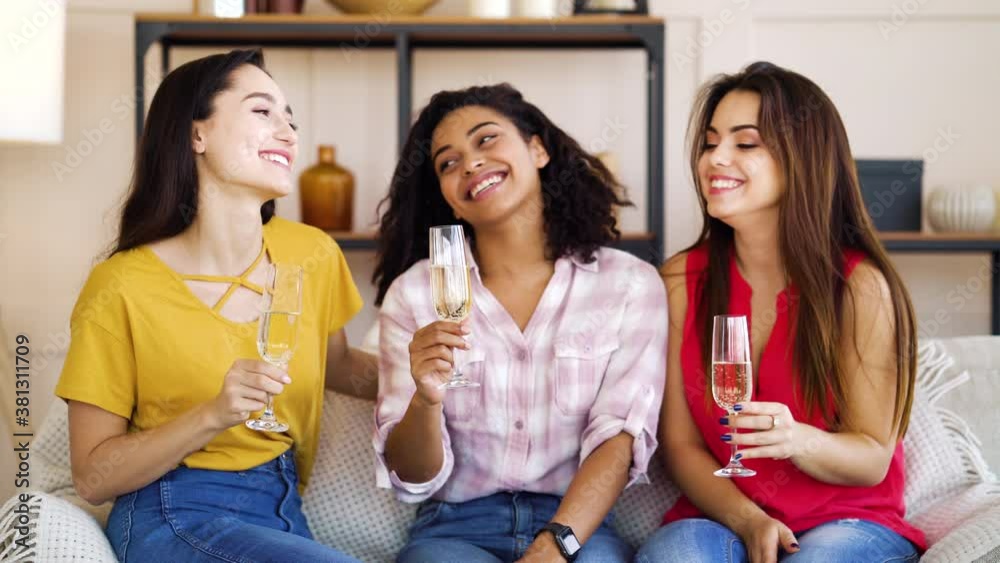 Group of multiracial women sitting on sofa in living room and drinking wine, toasting and smiling. Happy friends celebrating special occasion. Concept of holiday Group of multiracial women sitting on sofa in living room and drinking wine, toasting and smiling. Happy friends celebrating special occasion. Concept of holiday