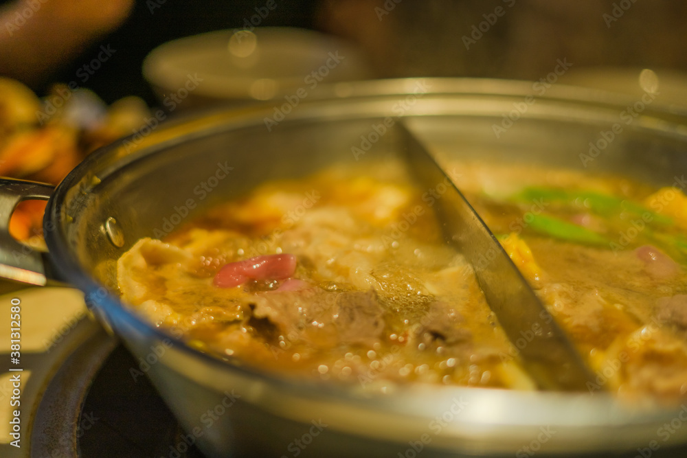 Hand using chopsticks pick raw sliced beef, vegetable, a piece of corn over the Chinese spicy hot pot, Szechuan Spicy Hot Pot Hand using chopsticks pick raw sliced beef, vegetable, a piece of corn over the Chinese spicy hot pot, Szechuan Spicy Hot Pot