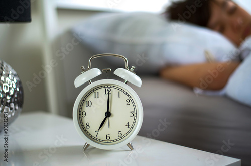  The alarm clock showing 7 am on the bedside table, The schoolboy happy sleepover on the weekend in the background.