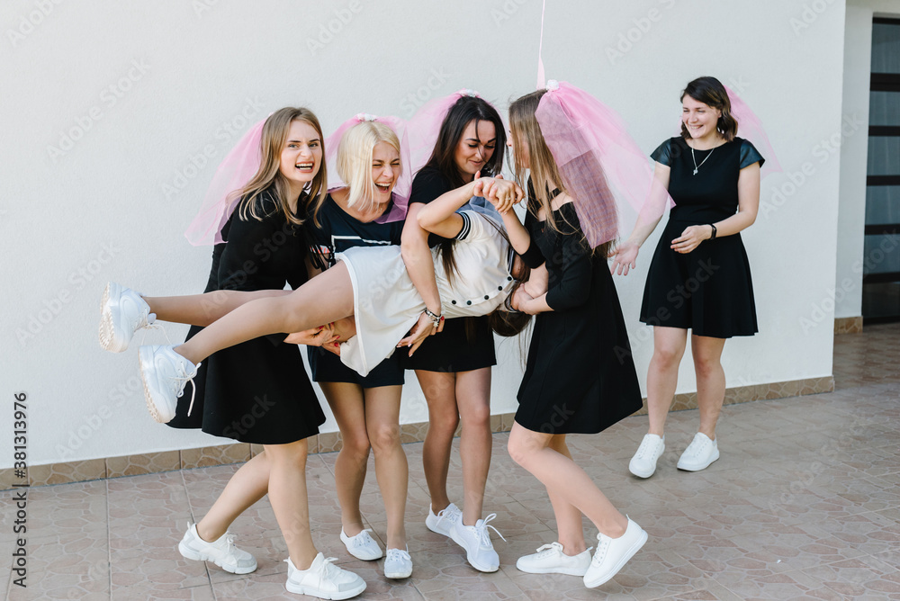Fototapeta premium Beautiful sexy young girls in dress and veil on bachelor party. Bride hugging bridesmaids smiling outdoors and celebrating bachelorette party. Maiden evening, Hen-parties. Place for text.