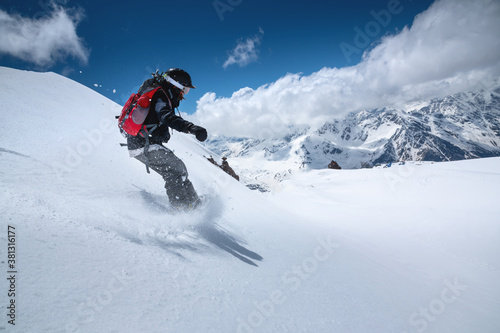Girl snowboarder with a backpack on a snowy fresh slope against the backdrop of high mountains and blue sky. Winter kinds of extreme sports. Snowboard
