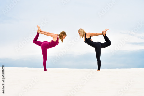 Two beautiful young women performing yoga pose nataradzhasana on the beach