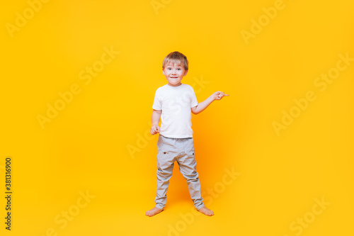 Cute boy on yellow background points with his hand to the side, photo for advertising product