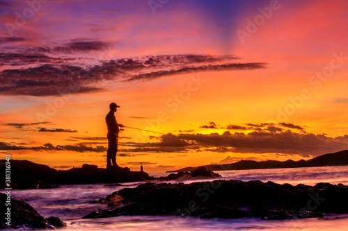 Traditional fisherman with fishing rod in hands at sunset sky burst