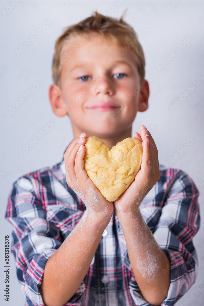 Cute boy holding in hands heart shaped piece of dough
