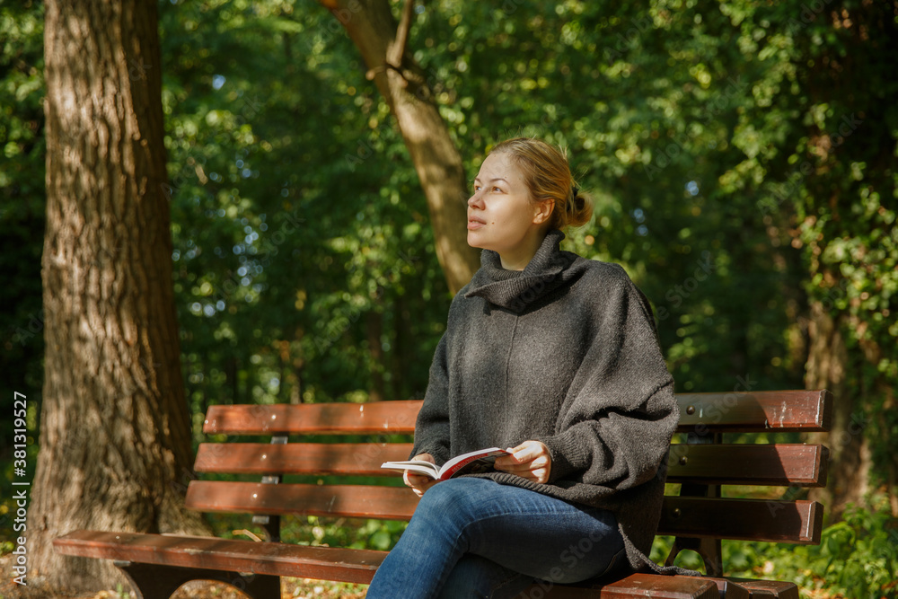 caucasian girl sits on bench in an autumn park with book