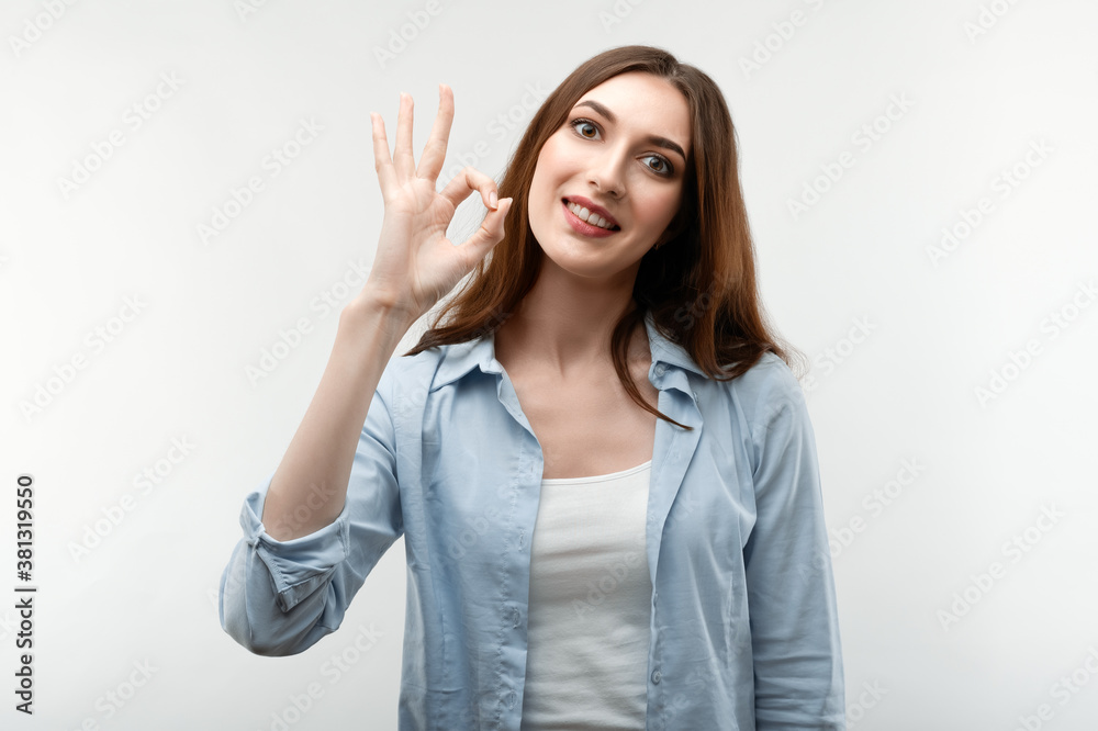Cheerful brunette girl looking at the camera with happy expression, showing OK gesture. Human emotions concept Cheerful brunette girl looking at the camera with happy expression, showing OK gesture. Human emotions concept