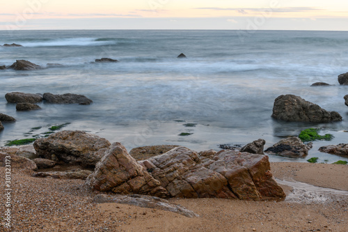Rocks on the beach in the evening with moving water which brings an effect to the surface of the sea.