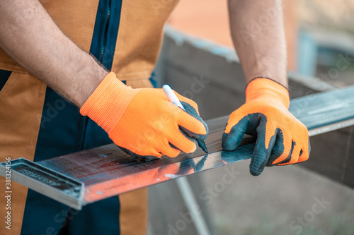 A carpenter in overalls marks the Board with a square and a permanent marker.