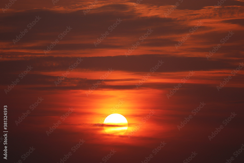 Sunset on colorful dramatic sky, orange sun shines through the clouds. Picturesque landscape for background