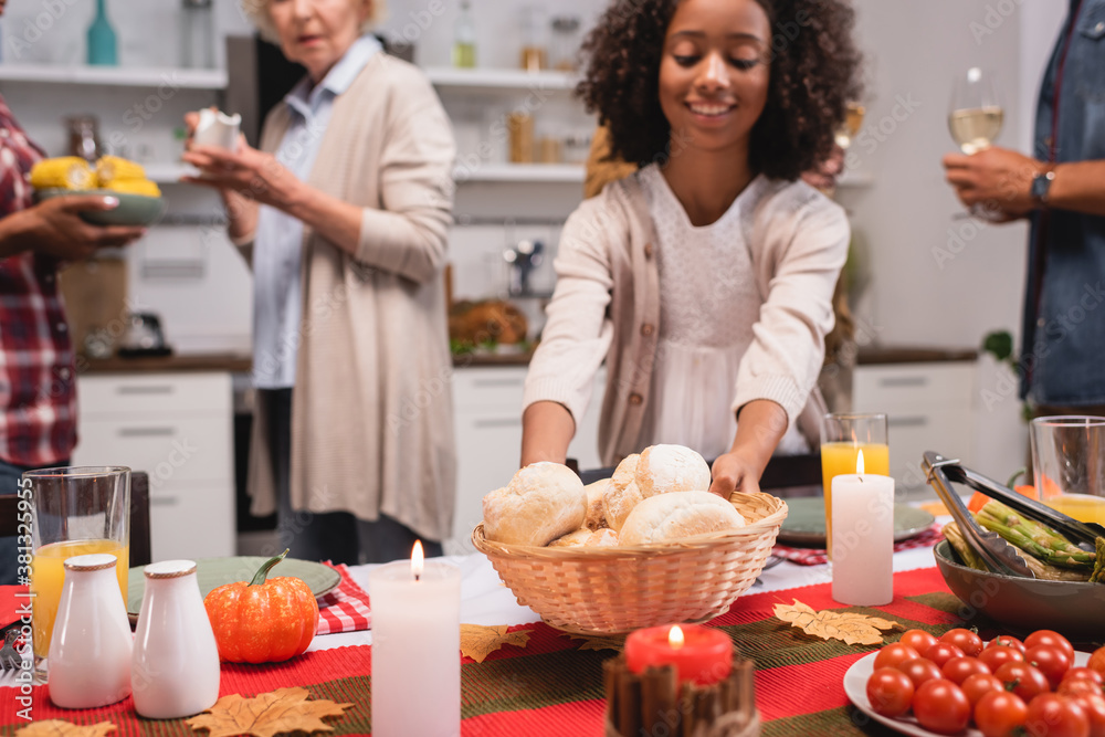 Selective focus of african american kid holding basket with buns near parents during thanksgiving dinner