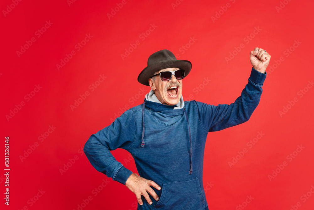Shouting, screaming. Portrait of senior man in stylish eyewear and hat isolated on red studio background. Tech and joyful elderly lifestyle concept. Trendy colors, forever youth. Copyspace for your ad Shouting, screaming. Portrait of senior man in stylish eyewear and hat isolated on red studio background. Tech and joyful elderly lifestyle concept. Trendy colors, forever youth. Copyspace for your ad