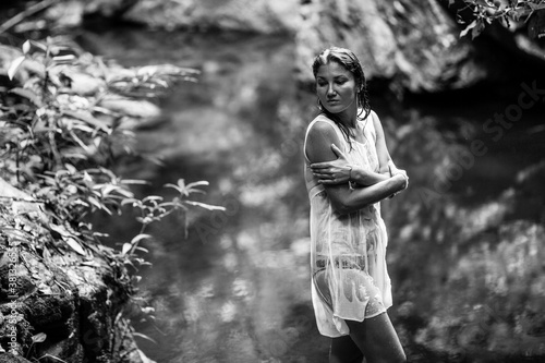 Woman sitting on the branches of a tree near the forest waterfall pond. Black and white photography.