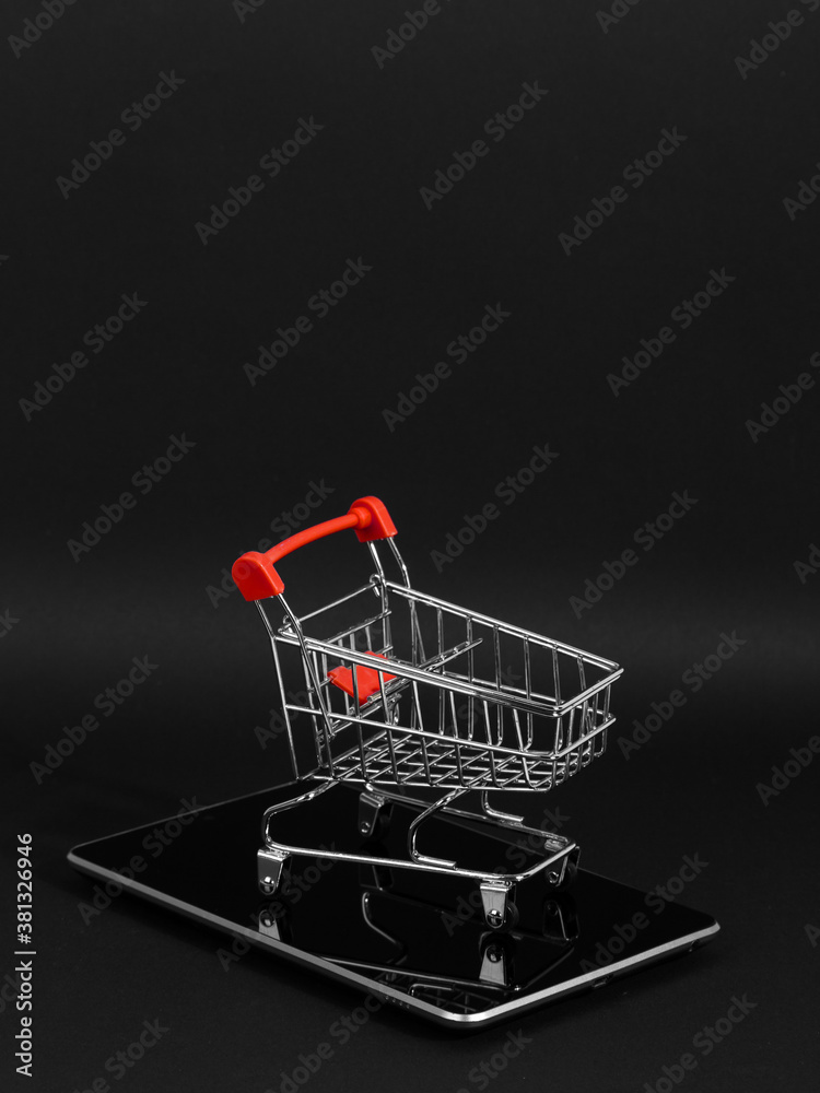 A tablet and shopping cart on a black background, a blank for the design, concept. Copy space.