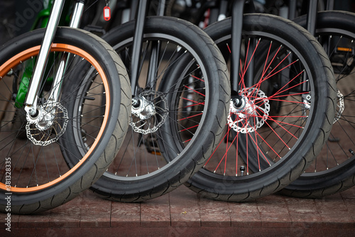 A close-up of the front wheels of a bicycle with disc brakes. Vintage city bicycles parked at a store or rental.