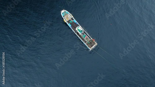 A fishing vessel equipped with a trawl catches fish in the open ocean. Aerial 4K shot.