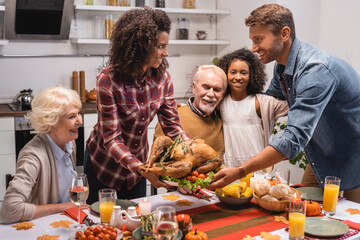 Selective focus of man taking turkey from african american wife near parents and daughter at table