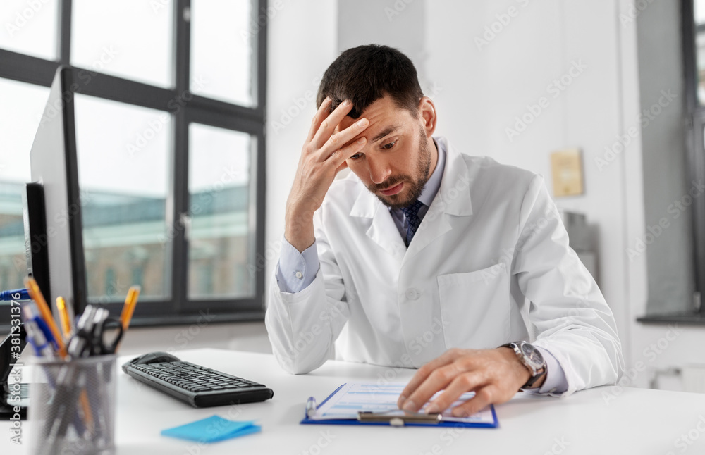 healthcare, medicine and people concept - stressed male doctor with clipboard at hospital healthcare, medicine and people concept - stressed male doctor with clipboard at hospital