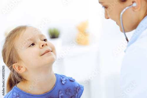 Doctor examining a little girl by stethoscope. Happy smiling child patient at usual medical inspection. Medicine and healthcare concepts