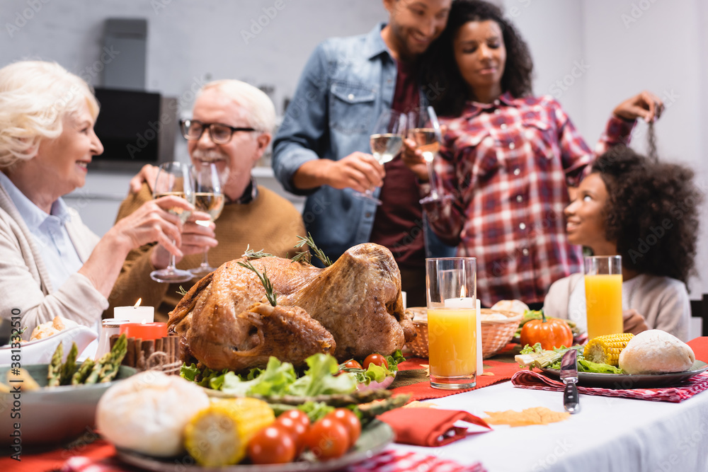 Selective focus of tasty turkey on table near multiethnic family with glasses of wine during thanksgiving celebration