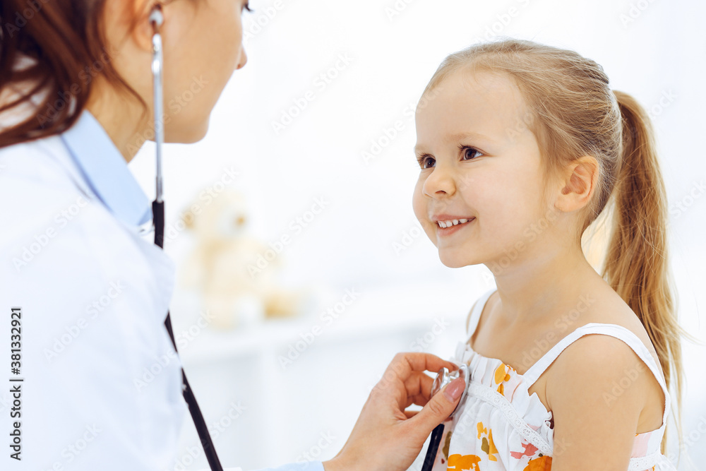 Doctor examining a little girl by stethoscope. Happy smiling child patient at usual medical inspection. Medicine and healthcare concepts Doctor examining a little girl by stethoscope. Happy smiling child patient at usual medical inspection. Medicine and healthcare concepts