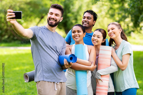 fitness, sport and healthy lifestyle concept - group of happy people with yoga mats taking selfie at park