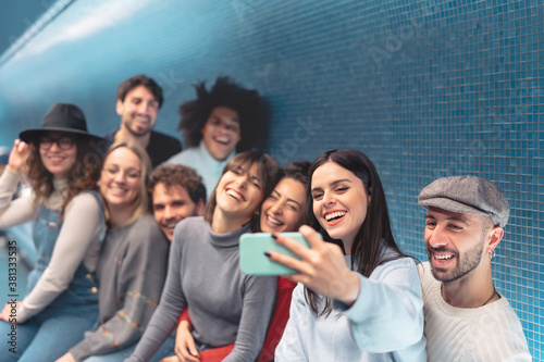 Group young friends taking selfie with mobile smartphone in subway underground metropolitan - Happy trendy people sharing time and laughing together - Youth millennial friendship lifestyle concept