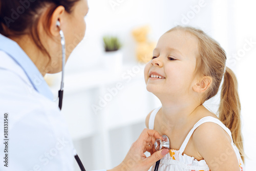 Doctor examining a little girl by stethoscope. Happy smiling child patient at usual medical inspection. Medicine and healthcare concepts