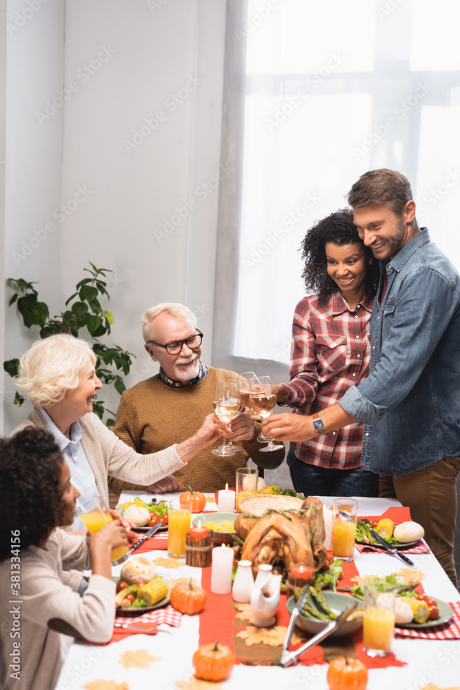 joyful multicultural family clinking wine glasses during thanksgiving dinner joyful multicultural family clinking wine glasses during thanksgiving dinner
