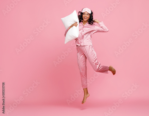 Excited woman in pajama jumping with pillow