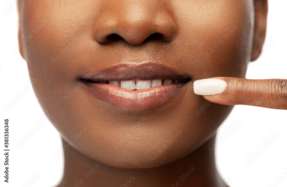 Naklejka premium beauty, dental care and people concept - close up of face of beautiful smiling young african american woman pointing to her mouth over white background