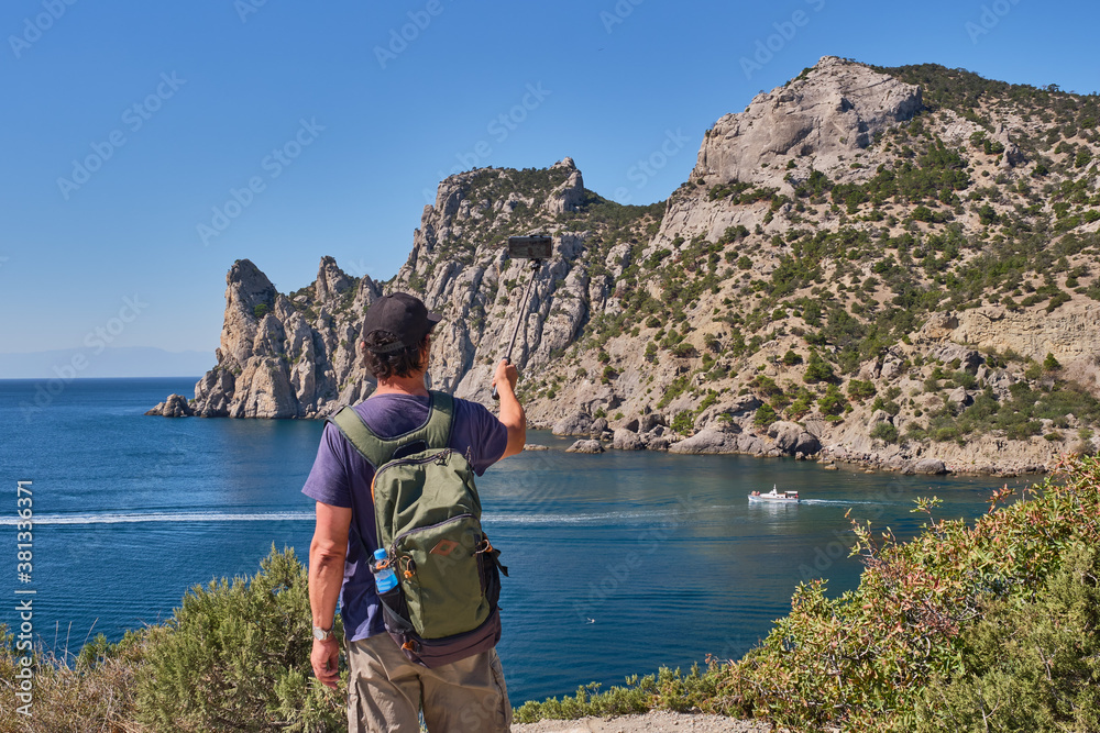 Black Sea coast, Crimea. An Asian elderly man takes photos over the background of the Blue Bay on the tourist route Golitsyn trail
