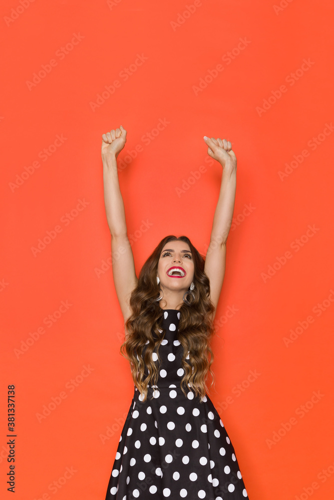 Young Woman In Elegant Cocktail Dress Is Standing With Arms Raised Looking Up And Laughing Young Woman In Elegant Cocktail Dress Is Standing With Arms Raised Looking Up And Laughing