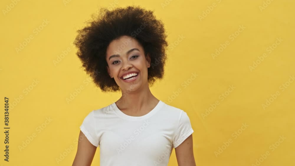 A smiling woman is pointing to the viewer standing isolated over a yellow background A smiling woman is pointing to the viewer standing isolated over a yellow background