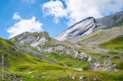 Sun shining onto rocky slopes and lush green meadows on the Tour Du Mont Blanc, French Alps